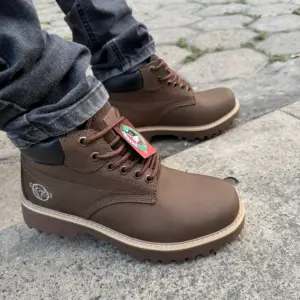 Botas Brahma de cuero marrón con suela dentada beige y cordones café, vistas de perfil sobre pavimento de piedra.